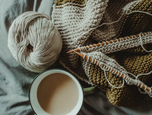 knitting supplies and cup of coffee placed on bed