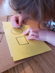 Yound child using a push pin to push holes along traces shapes.