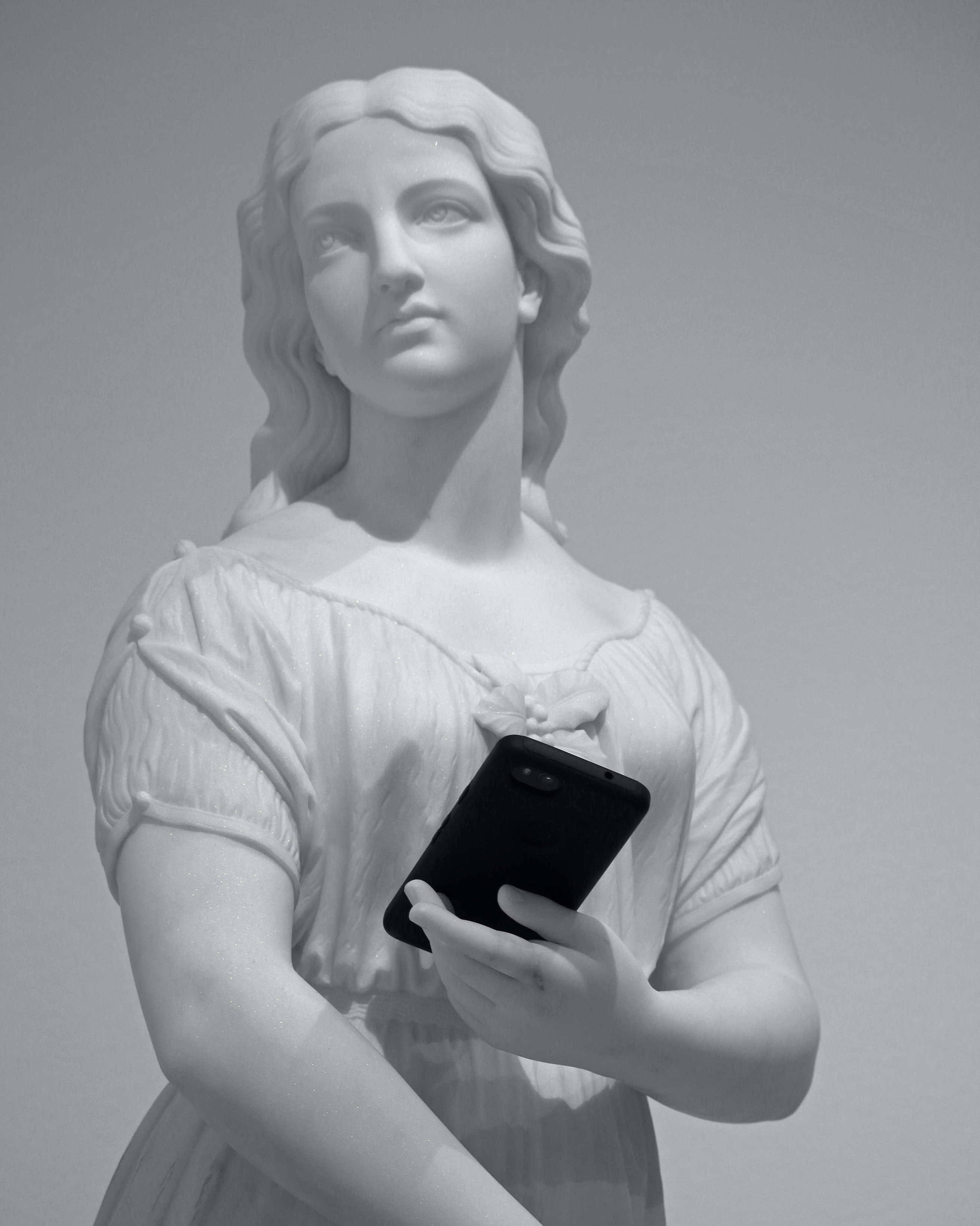 Statue with cell phone placed in the palm of her hands.