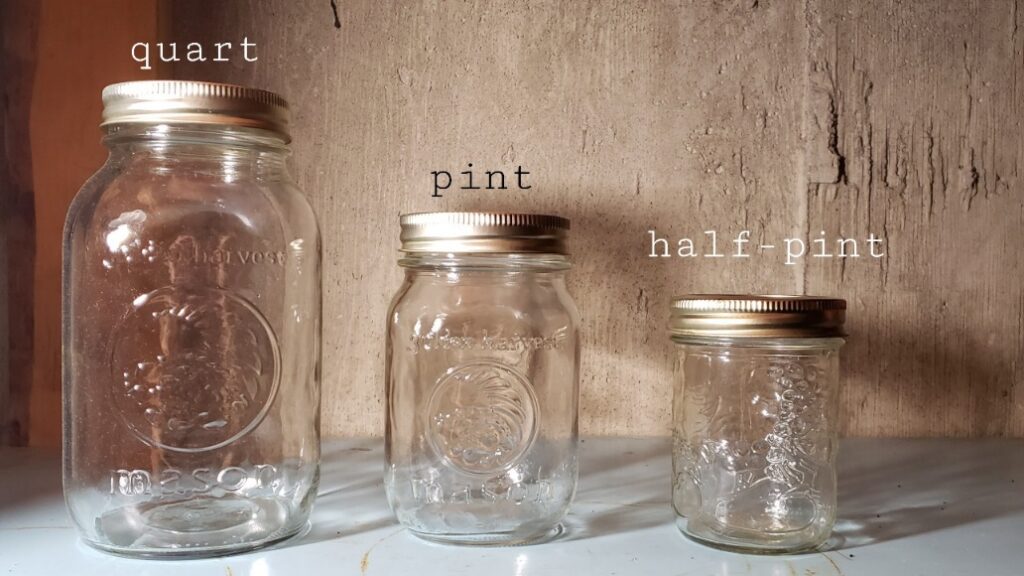 Mason jars of quart, pint and half-pint on a shelf against a concrete wall.